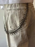 Spike pants chain worn over back pocket of beige jeans